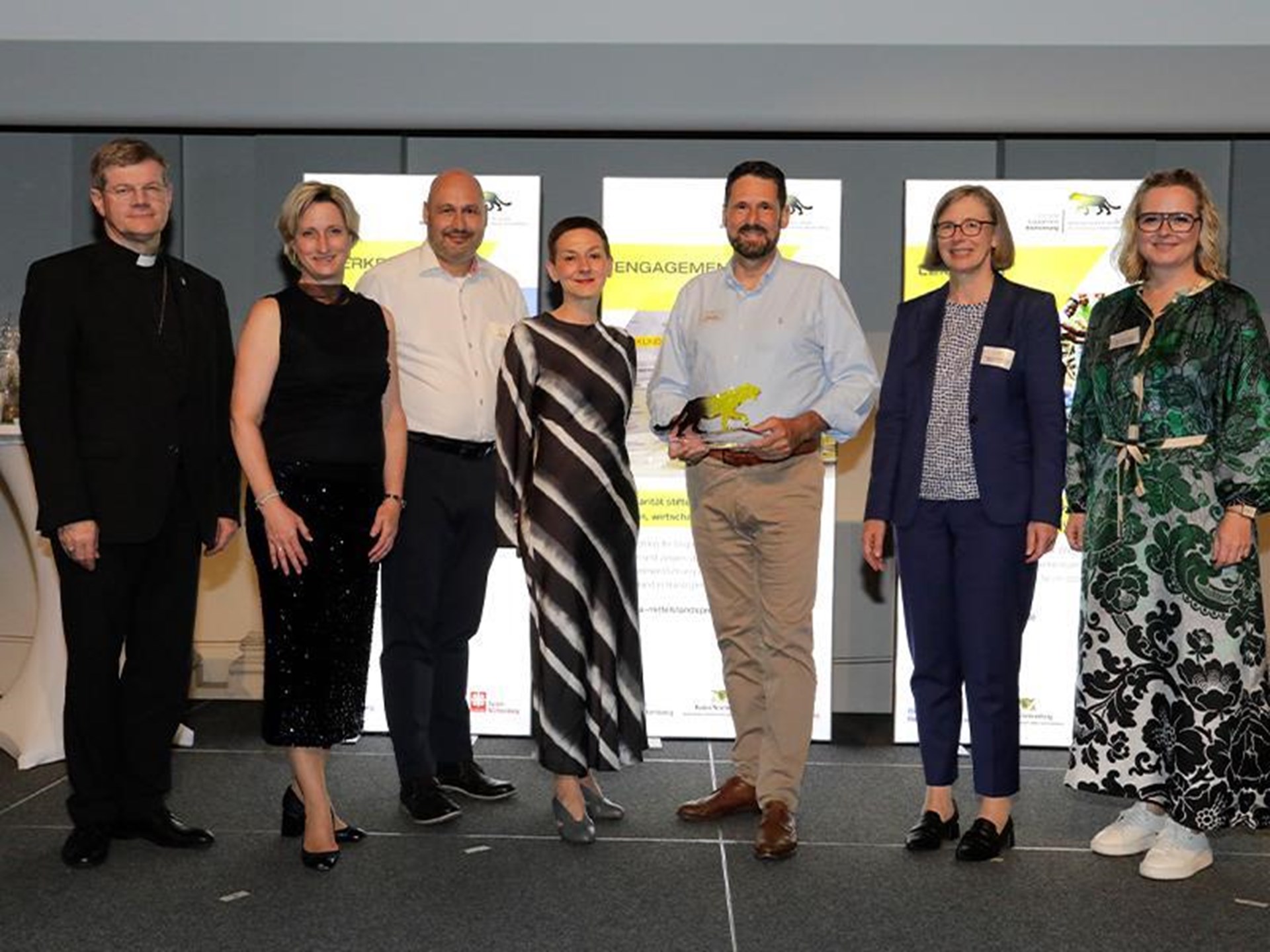 Gruppenfoto von sieben Personen auf Bühne, Person in der Mitte hält Trophäe in Form eines Panthers