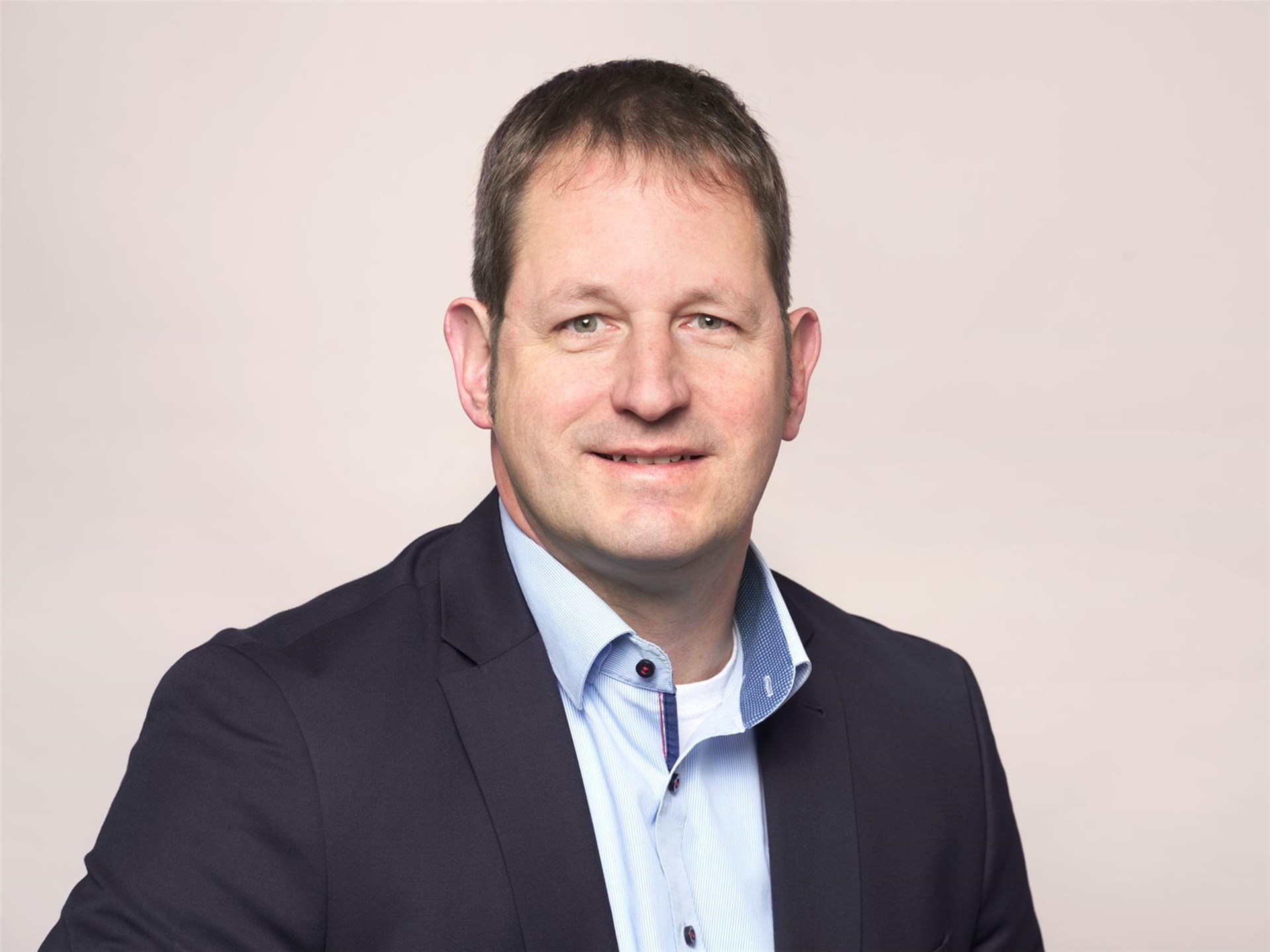 Mann mit kurzen dunklen Haar mit blauen Hemd und marineblauen Sakko.