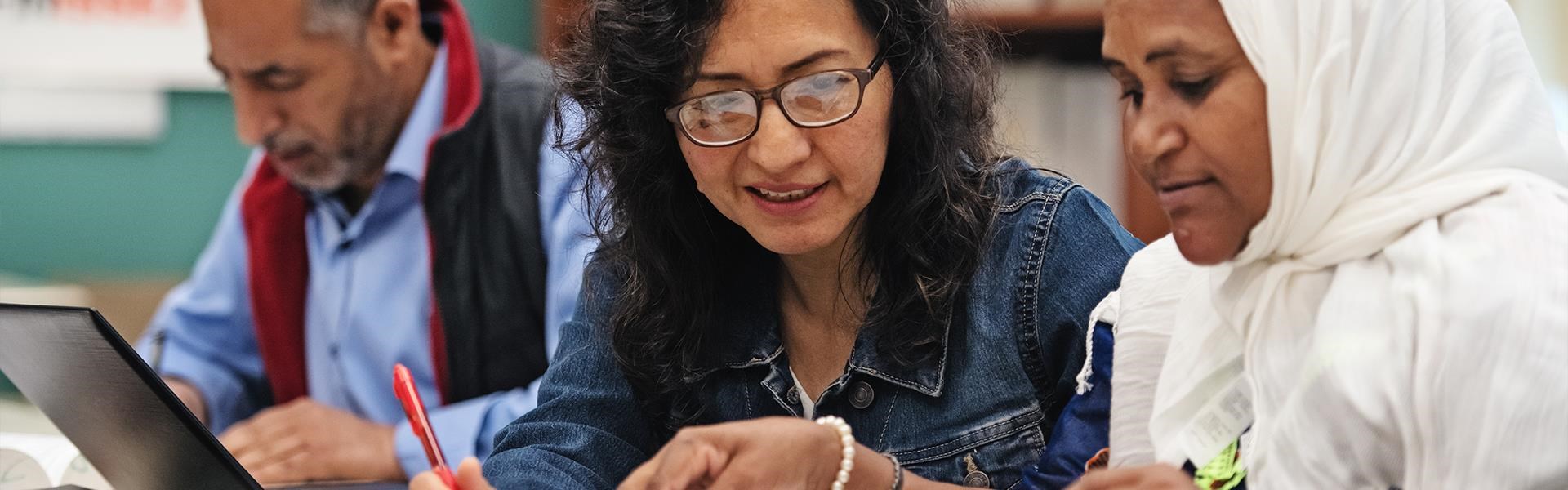 Drei Personen mit unterschiedlichem Hintergrund arbeiten gemeinsam an einem Tisch mit Laptops und Unterlagen