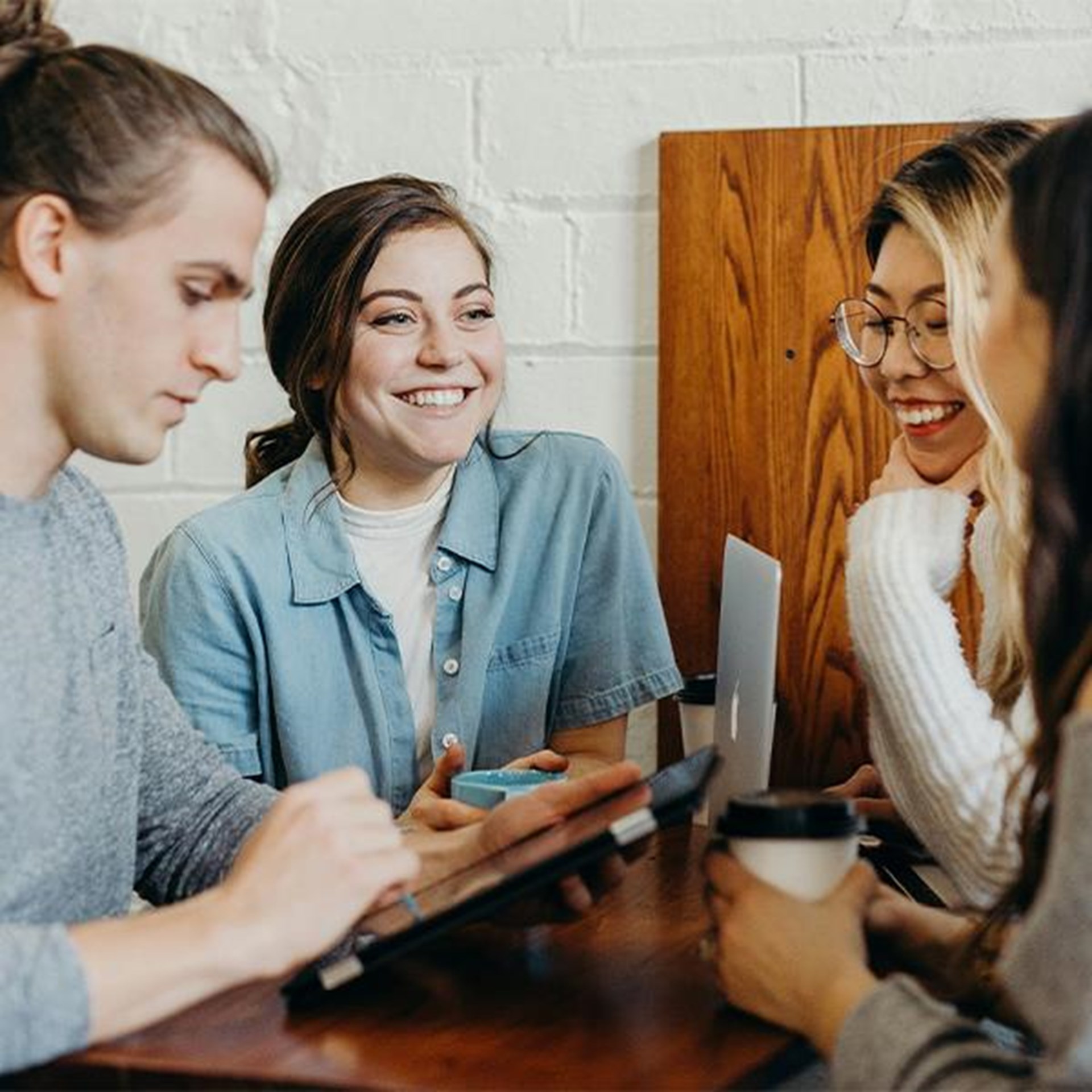 Vier junge Personen sitzen gemeinsam an einem Tisch, arbeiten zusammen und unterhalten sich