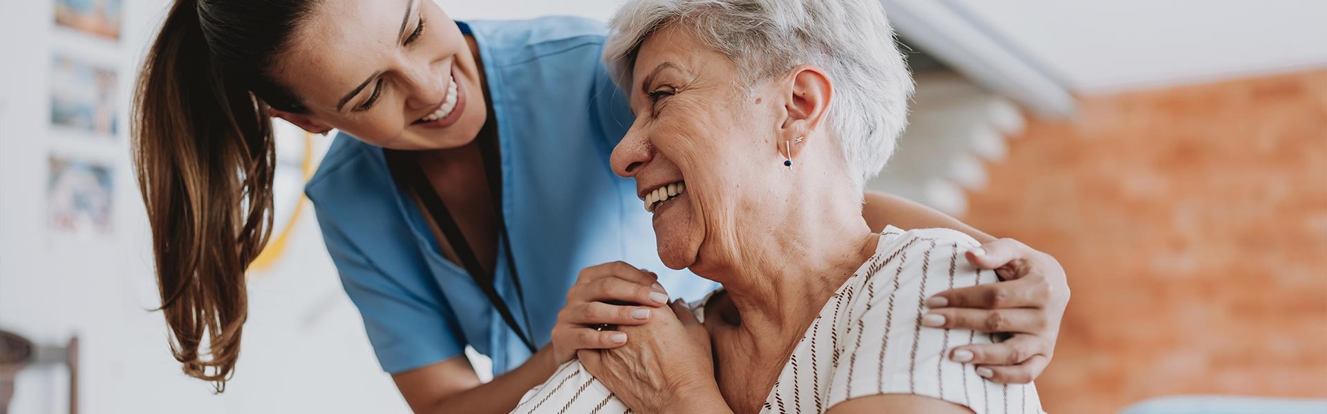 Pflegekraft und ältere Person lachen gemeinsam in heller Umgebung, vermittelt Nähe und Freude in der Pflege